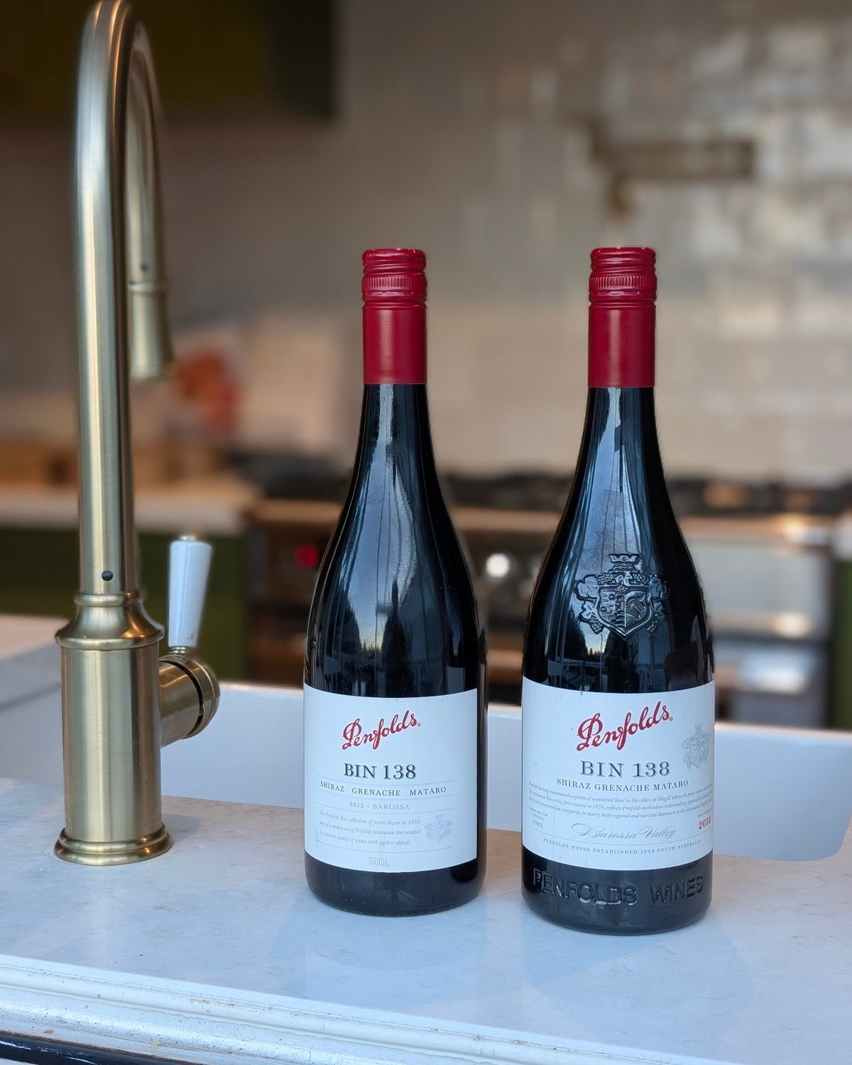 Two bottles of Penfolds Bin 138, 2012 and 2018, on a marble kitchen bench beside a brass tap